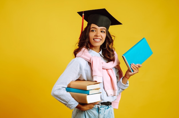 Mulher de graduação com um chapéu de formatura na cabeça, com livros em amarelo.