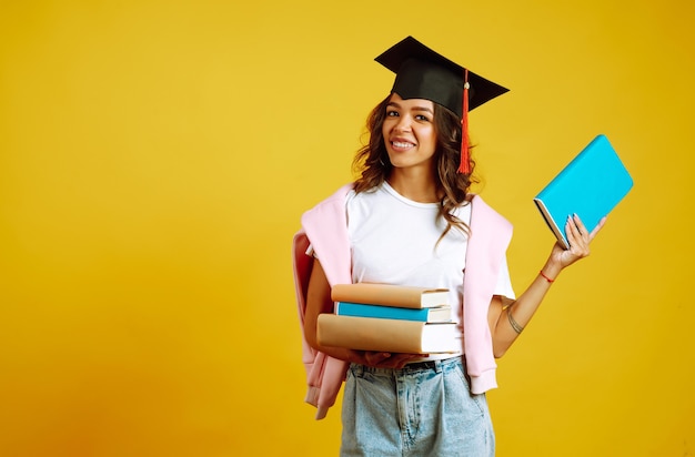 Mulher de graduação com um chapéu de formatura na cabeça, com livros em amarelo.