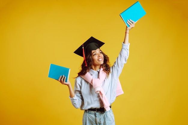 Mulher de graduação com um chapéu de formatura na cabeça, com livros em amarelo.