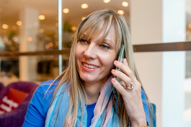 Mulher de idade em uma blusa azul e cachecol tomando café no café e conversando