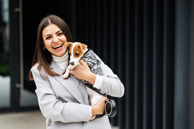 Mulher de jaqueta casual abraçando seu cão de raça pura Jack Russell Terrier treinado favorito vestido de terno para cães ao ar livre em dia de outono