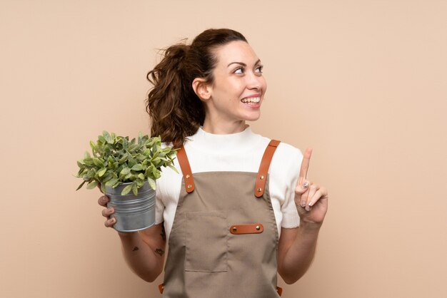 Mulher de jardineiro segurando uma planta com a intenção de realizar a solução enquanto levanta um dedo