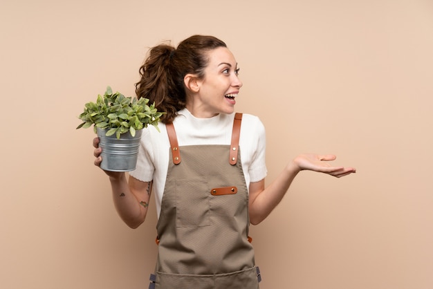 Mulher de jardineiro segurando uma planta com expressão facial de surpresa