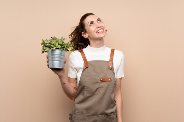 Mulher de jardineiro segurando uma planta olhando para cima enquanto sorrindo