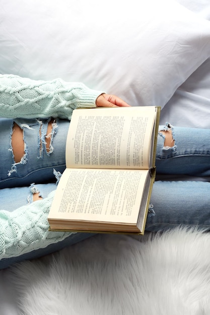 Mulher de jeans azul lendo livro no ponto de vista superior da cama