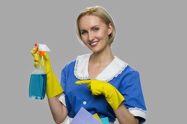 Mulher de limpeza de uniforme apresentando detergente. Governanta bonita mostrando o frasco de química para limpeza. Anúncio de spray mais limpo.