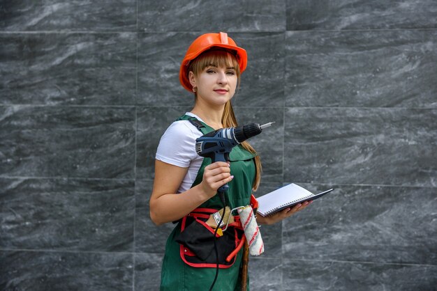 Mulher de macacão de proteção e capacete segurando uma chave de fenda e um diário em abstrato