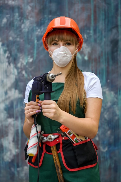 Mulher de macacão verde e máscara protetora segurando a máquina de perfuração em fundo abstrato