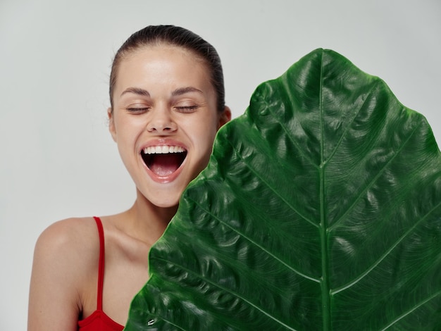 Mulher de maiô vermelho rindo com a boca bem aberta e a pele limpa de palmeira de folhas verdes