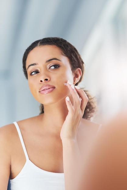 Mulher de manhã e cuidado da pele com creme em casa para tratamento facial brilho da pele e aplicação modelo de banheiro feminino e hidratante para o rosto com cosméticos colágeno e rotina para beleza