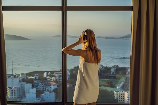 Foto mulher de manhã ouve fones de ouvido sem fio no fundo de uma janela com vista para o mar