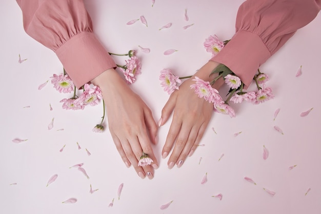 Mulher de mãos de beleza com flores cor de rosa está na mesa. Cosmético natural para cuidados com a pele das mãos. Unhas perfeitas