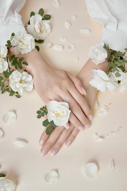 Mulher de mãos de beleza com flores rosas está em cima da mesa. Cosmético natural para cuidados com a pele das mãos. Maquiagem fashion