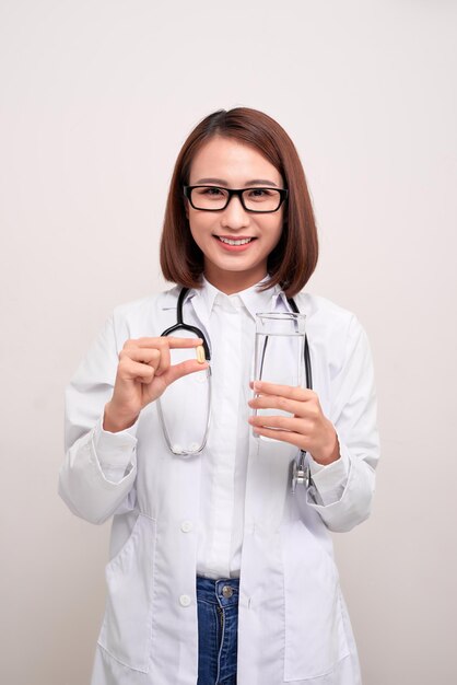 Mulher de médico segurando água e remédios em fundo branco.