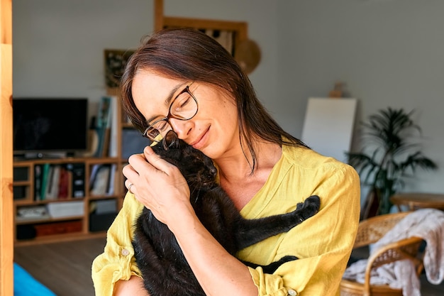Mulher de meia-idade abraçando um lindo gato preto na cena interna Relações entre humanos e animais