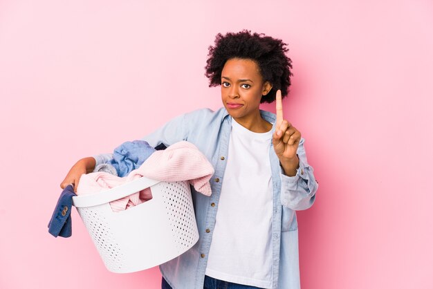 Mulher de meia-idade afro-americana lavando roupa isolada mostrando o número um com o dedo.