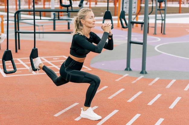 Mulher de meia-idade agachada bombeando massa muscular no campo de esportes
