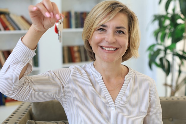 Mulher de meia idade alegre, agente imobiliário, sentado no sofá, segurando as chaves da nova casa.