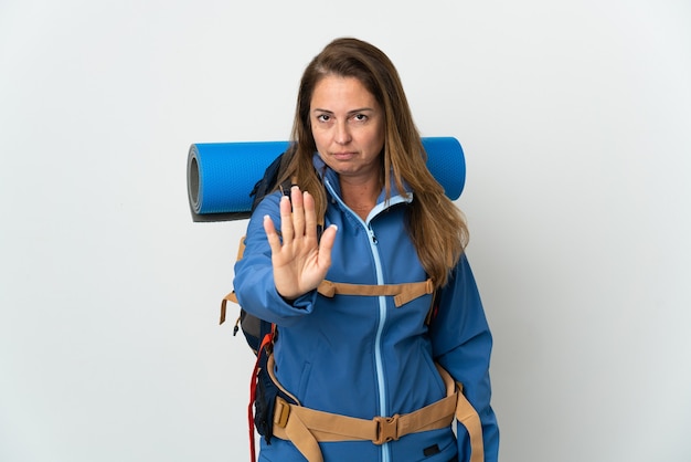 Mulher de meia-idade, alpinista com uma grande mochila sobre uma parede isolada, fazendo gesto de pare