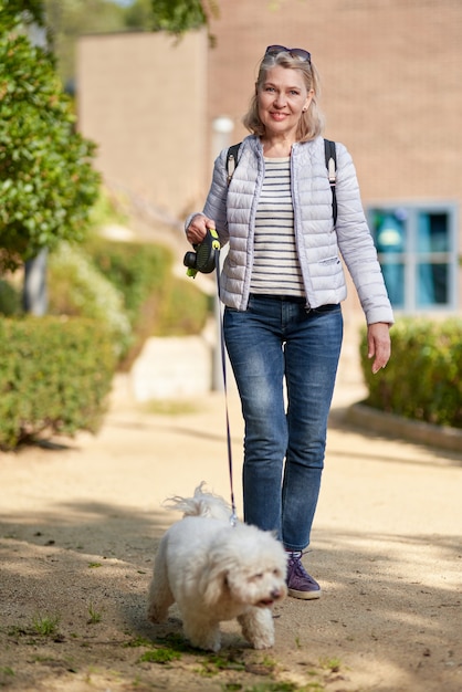 Mulher de meia-idade andando com cachorro branco fofo na cidade de verão.