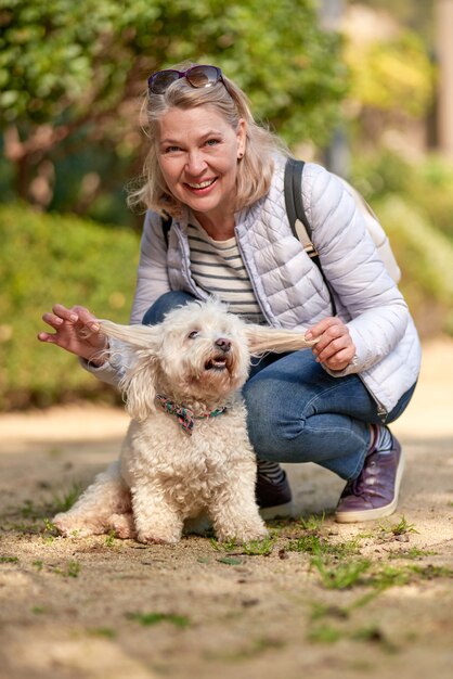 Mulher de meia-idade andando com cachorro branco fofo na cidade de verão.