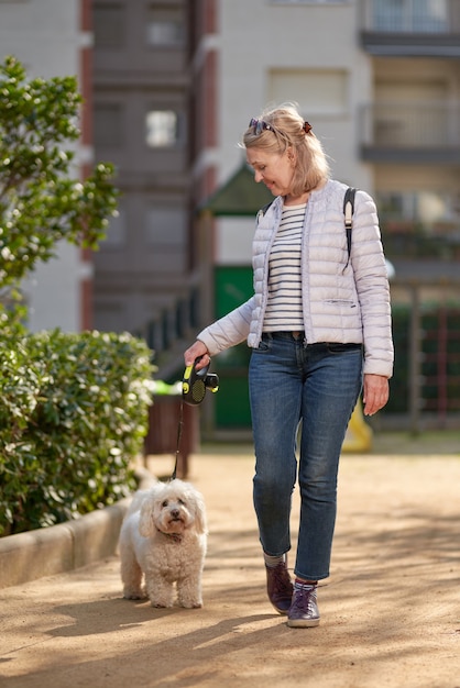 Mulher de meia-idade andando com cachorro branco fofo na cidade de verão.