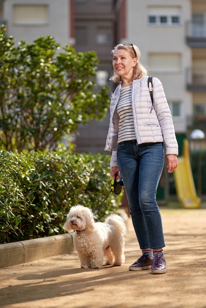 Foto mulher de meia-idade andando com cachorro branco fofo na cidade de verão.