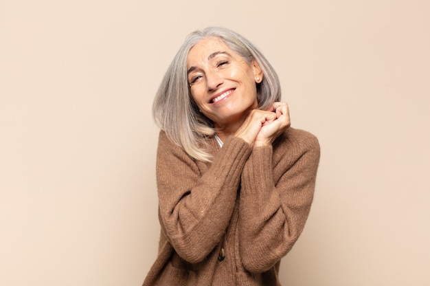 Mulher de meia-idade apaixonada e bonita, adorável e feliz, sorrindo romanticamente com as mãos ao lado do rosto