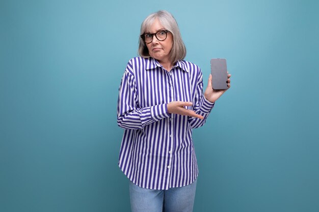 mulher de meia idade aposentada moderna com cabelos grisalhos está estudando gadget de smartphone em fundo de estúdio brilhante com copyspace