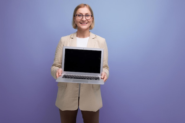 Mulher de meia-idade bem-sucedida em jaqueta com laptop para trabalhar no fundo do estúdio com espaço de cópia