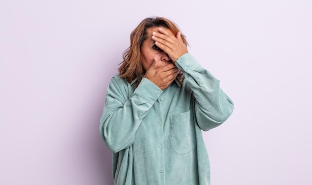 Mulher de meia-idade cobrindo o rosto com as duas mãos dizendo não para a câmera! recusando fotos ou proibindo fotos