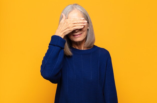 Mulher de meia-idade cobrindo os olhos com uma das mãos, sentindo-se assustada ou ansiosa, imaginando ou esperando cegamente por uma surpresa