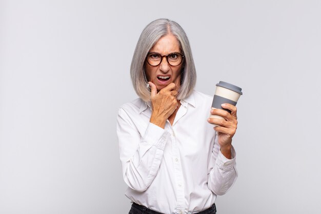 Mulher de meia-idade com boca e olhos bem abertos e mão no queixo, sentindo-se desagradavelmente chocada, dizendo o que ou uau conceito de café