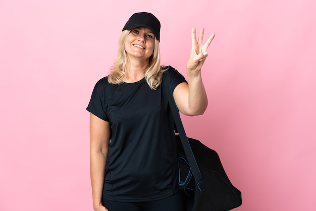 Mulher de meia-idade com bolsa esporte isolada feliz na parede rosa contando três com os dedos