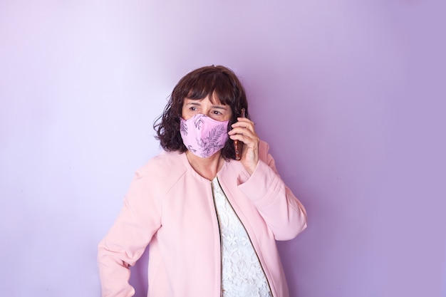 Foto mulher de meia-idade com cabelo encaracolado e máscara médica rosa usando um telefone celular em um fundo rosa