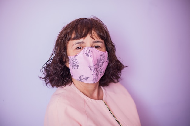 Mulher de meia-idade com cabelo encaracolado usando máscara rosa sobre fundo rosa