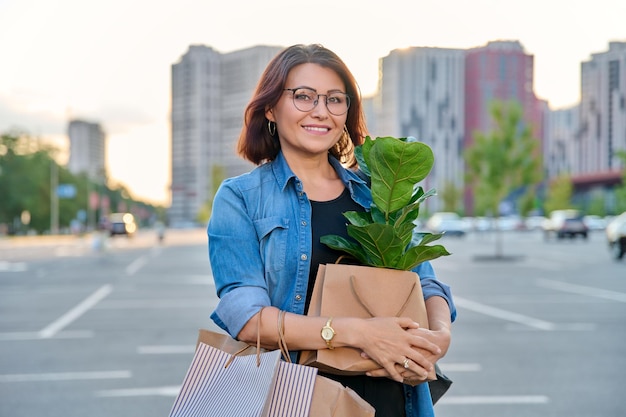 Foto mulher de meia idade com sacolas de papel com compra de planta olhando para a câmera