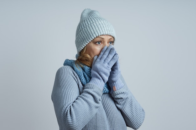 Mulher de meia-idade com um chapéu cinza, suéter, luvas, esconde o nariz do frio