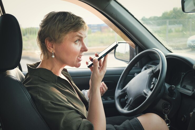 Mulher de meia idade com um corte de cabelo curto senta-se ao volante de um carro e fala indignada ao telefone