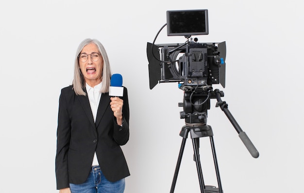 Mulher de meia-idade de cabelo branco gritando agressivamente, parecendo muito zangada e segurando um microfone. conceito de apresentador de televisão