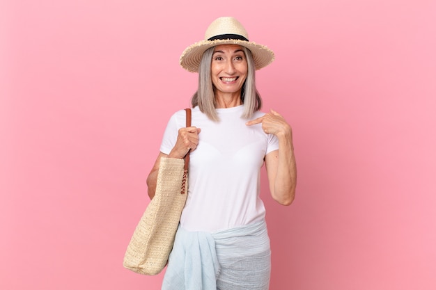 Mulher de meia-idade de cabelo branco parecendo chocada e surpresa com a boca bem aberta, apontando para si mesma. conceito de verão