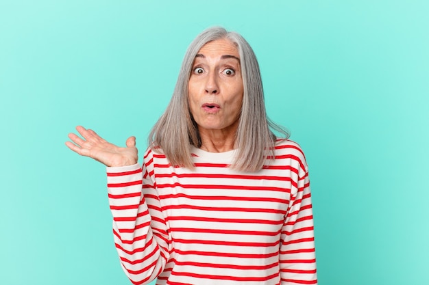 Mulher de meia-idade de cabelo branco parecendo surpresa e chocada, com o queixo caído segurando um objeto