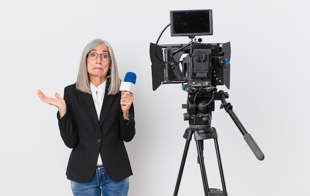 Mulher de meia-idade de cabelo branco se sentindo perplexa e confusa, duvidando e segurando um microfone. conceito de apresentador de televisão