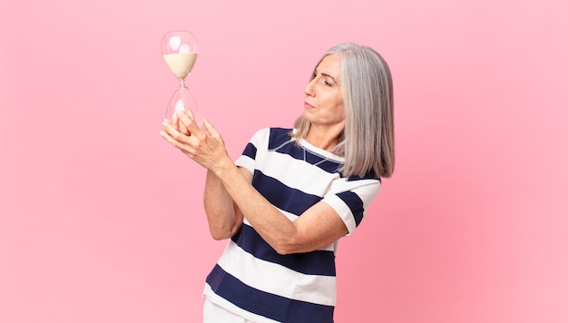 Mulher de meia-idade de cabelo branco segurando um cronômetro de ampulheta