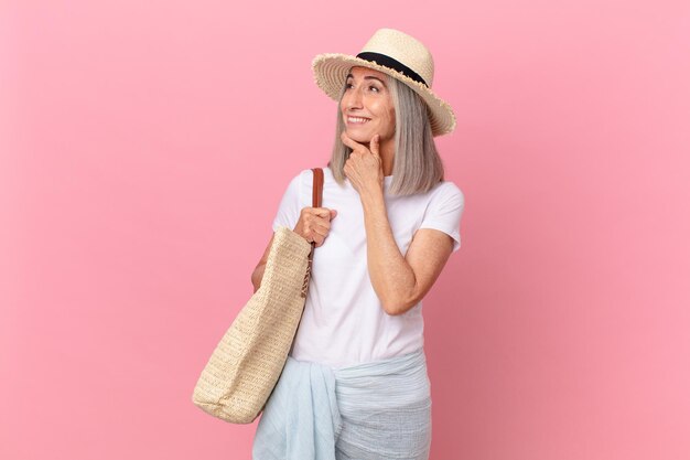 Mulher de meia-idade de cabelo branco sorrindo com uma expressão feliz e confiante com a mão no queixo. conceito de verão