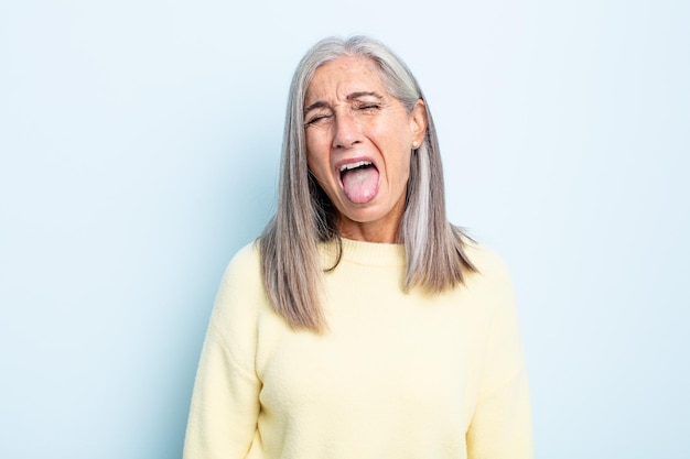 Mulher de meia-idade de cabelos grisalhos com atitude alegre, despreocupada e rebelde, brincando e mostrando a língua, se divertindo