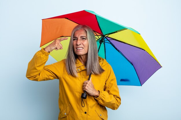 Mulher de meia-idade de cabelos grisalhos se sentindo confusa e perplexa, mostrando que você é louco. conceito de guarda-chuva e chuva