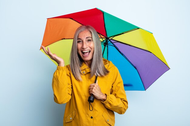 Mulher de meia-idade de cabelos grisalhos se sentindo feliz e surpresa com algo inacreditável. conceito de guarda-chuva e chuva