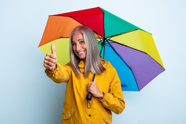 Mulher de meia-idade de cabelos grisalhos se sentindo orgulhosa, sorrindo positivamente com o polegar para cima. conceito de guarda-chuva e chuva