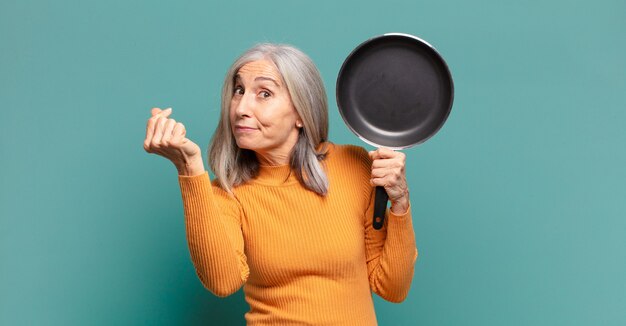 Mulher de meia-idade e cabelos grisalhos, bonita, aprendendo a cozinhar com uma panela